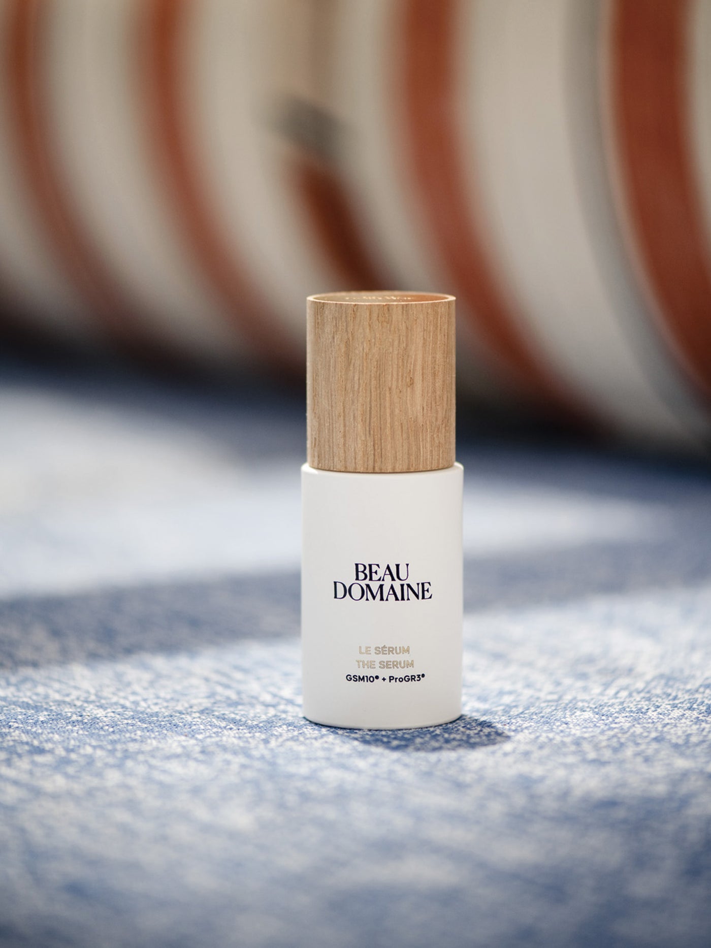 Beau Domaine skincare bottle with wooden cap on a textured surface